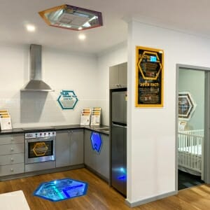 Exhibit kitchen with hexagon panels on wall, floor and ceiling; fridge and crib
