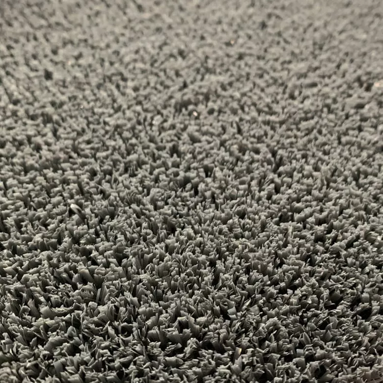 Close-up of a gray faux grass texture, showing dense, short strands densely packed together. The surface appears uniform and slightly rough