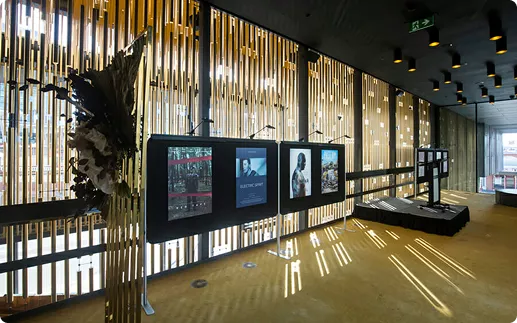 Modern gallery with three digital screens displaying movie posters. Bamboo slats and soft lighting create a warm, inviting ambiance.