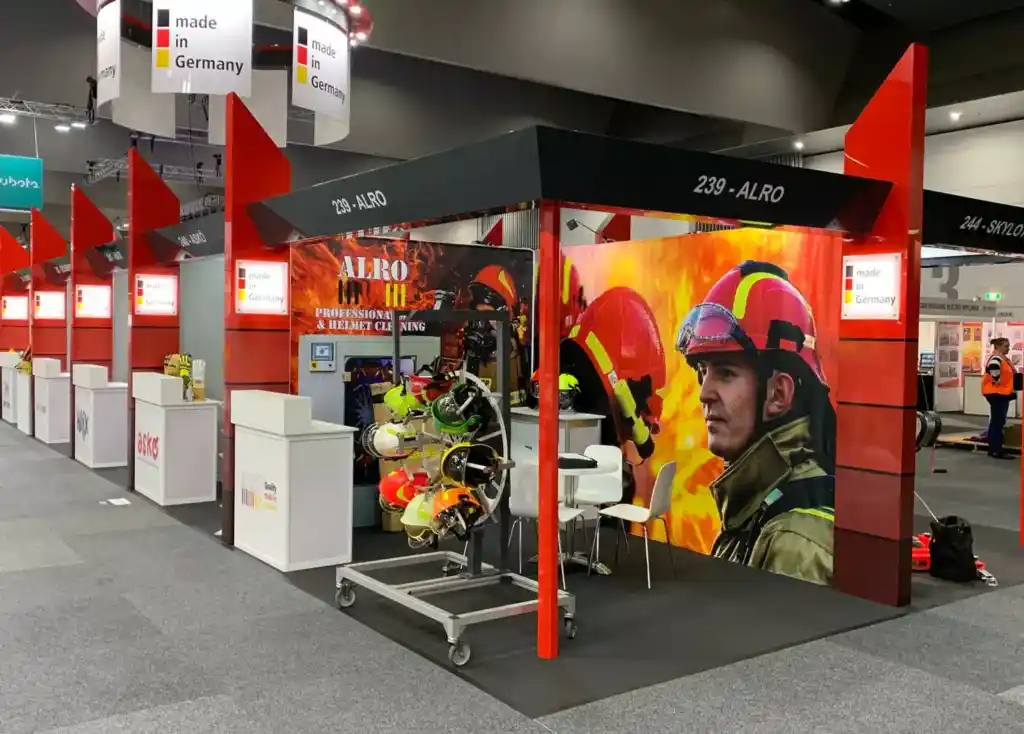 Trade show booth for Ziegler Group with fire safety equipment on display. Features a vivid firefighter mural and German flag elements