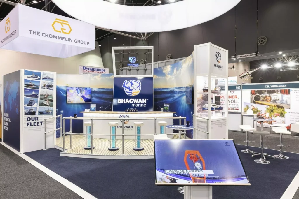 Exhibition booth for Bhagwan Marine with a central counter, large logo, and ocean-themed graphics. Adjacent stands feature various marine industry displays