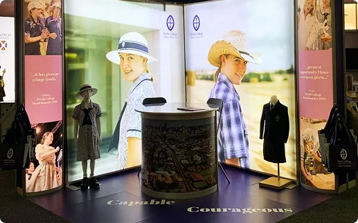 Trade show booth with illuminated panels showing people wearing hats and smiling outdoors. Mannequins display historical uniforms.