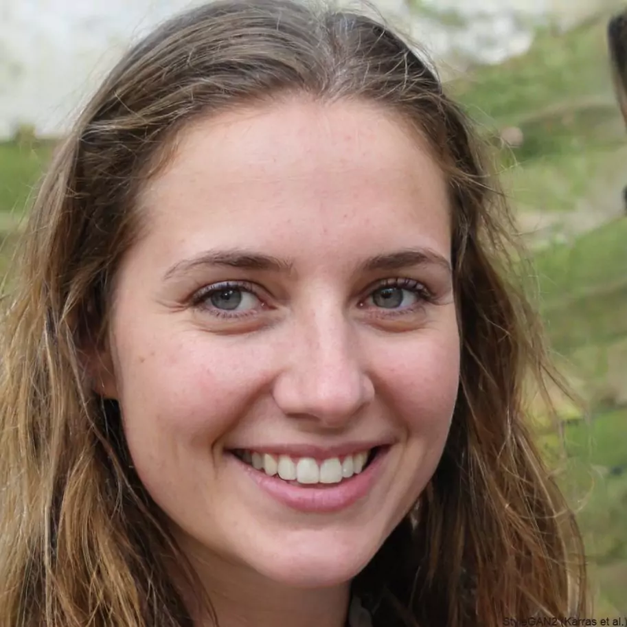 Smiling woman with shoulder-length brown hair and blue eyes in an outdoor setting. The background is blurred, conveying a warm, friendly atmosphere