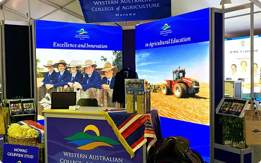 Exhibition booth for Western Australian College of Agriculture, featuring agricultural students, a tractor, and a vibrant display promoting education.