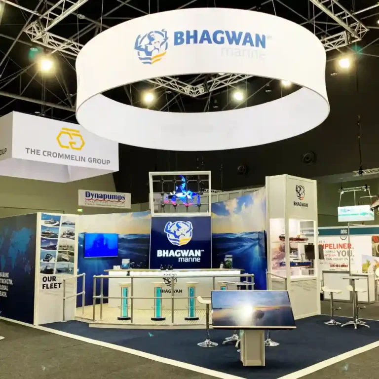 Exhibition booth for Bhagwan Marine with a suspended circular banner, blue ocean graphics, digital screens, and bar stools on a carpeted floor.