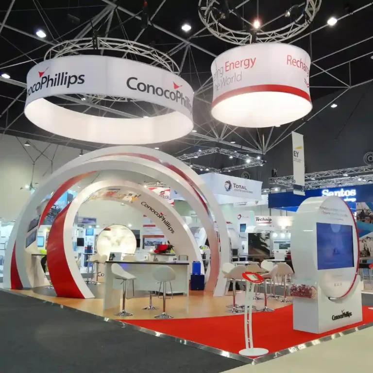 Trade show booth with ConocoPhillips branding features large circular displays, modern white and red design, sleek furniture, and an interactive screen.