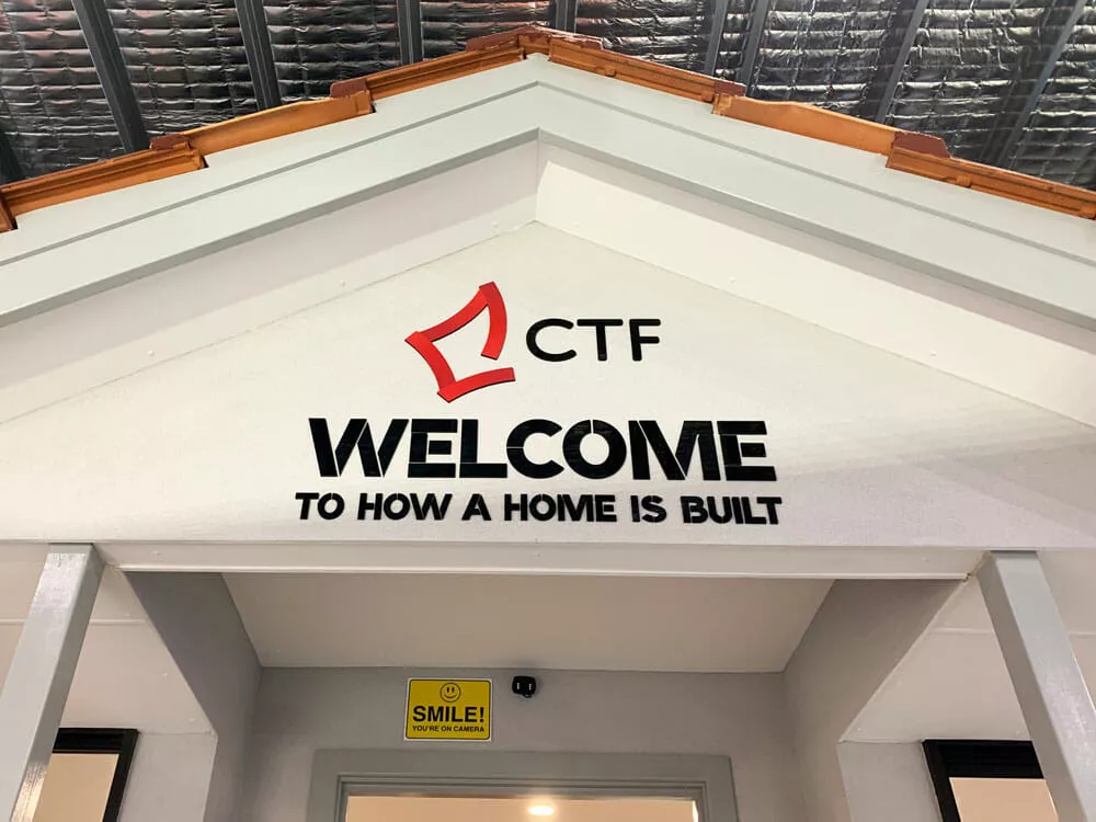 Entrance facade with a peaked roof features 'CTF Welcome to How a Home is Built' in bold letters, conveying a theme of construction and learning.