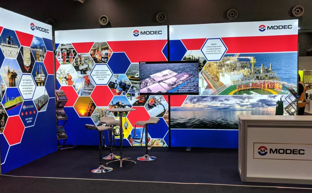 Trade show booth designed by Barrett Exhibition Group Perth for Modec, featuring red, blue, and white hexagonal designs with table and stools.