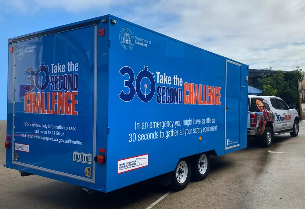 Bright blue trailer with "30 Second Challenge" safety message, connected to a white vehicle. Promotes rapid emergency preparedness for marine safety