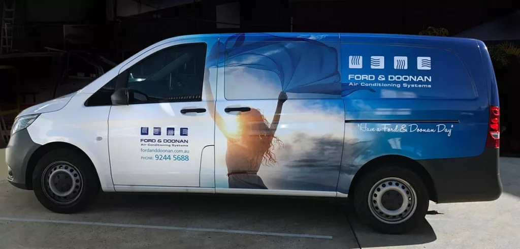 A white van with a colorful wrap displays a person holding a fabric against a sunset. Branding and details for Ford & Doonan Air Conditioning Systems are visible