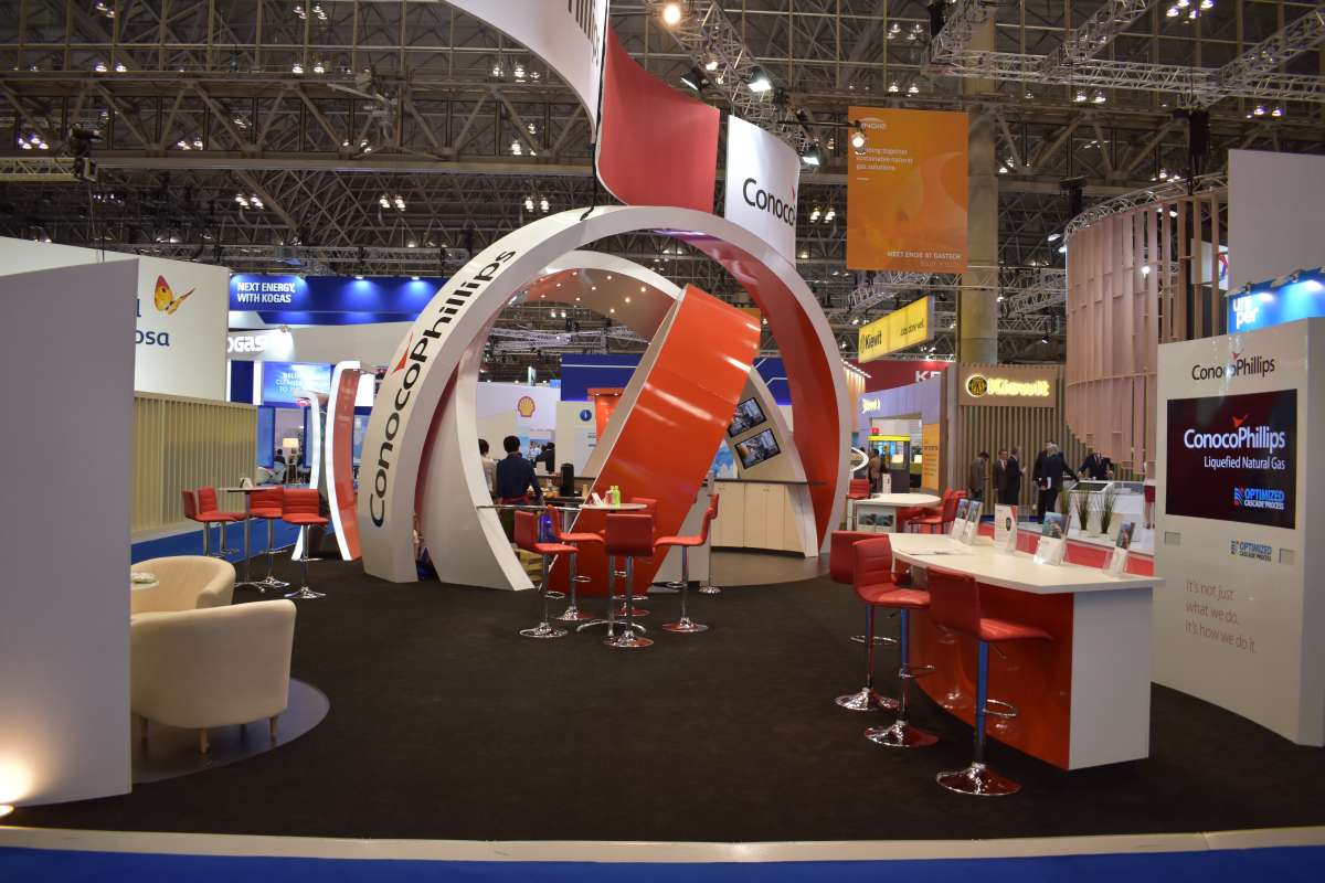 Trade show booth with red and white curved structures, ConocoPhillips branding, sleek red bar stools, digital screens, and a modern, inviting atmosphere.