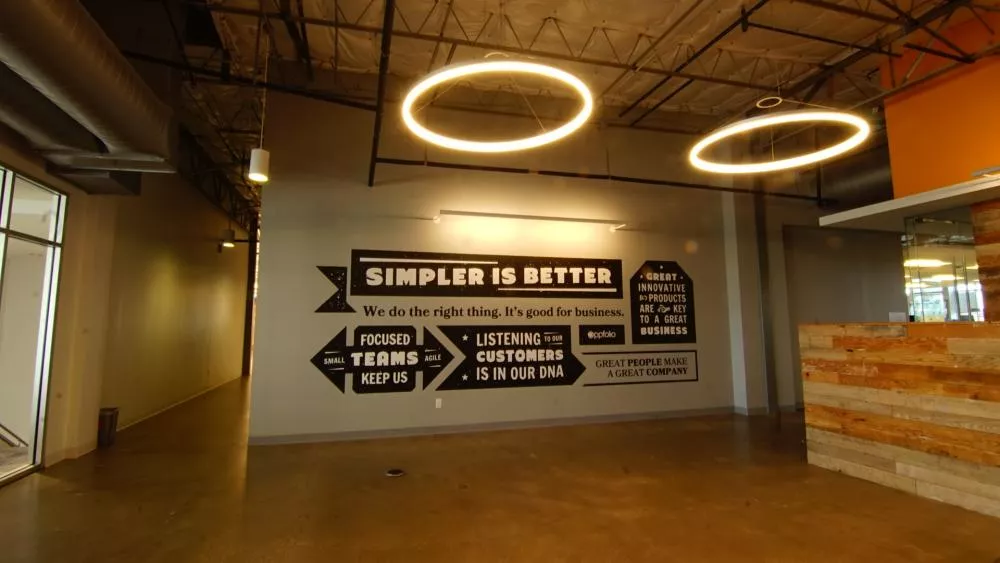 Industrial-style office with motivational wall art stating "Simpler is Better." Modern circular lights hang from the ceiling, creating a warm, inviting ambiance