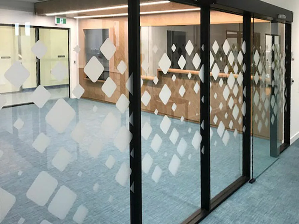 Glass sliding doors with a frosted diamond pattern, opening into a bright, modern room with light blue carpet and wood-paneled walls, creating a professional feel