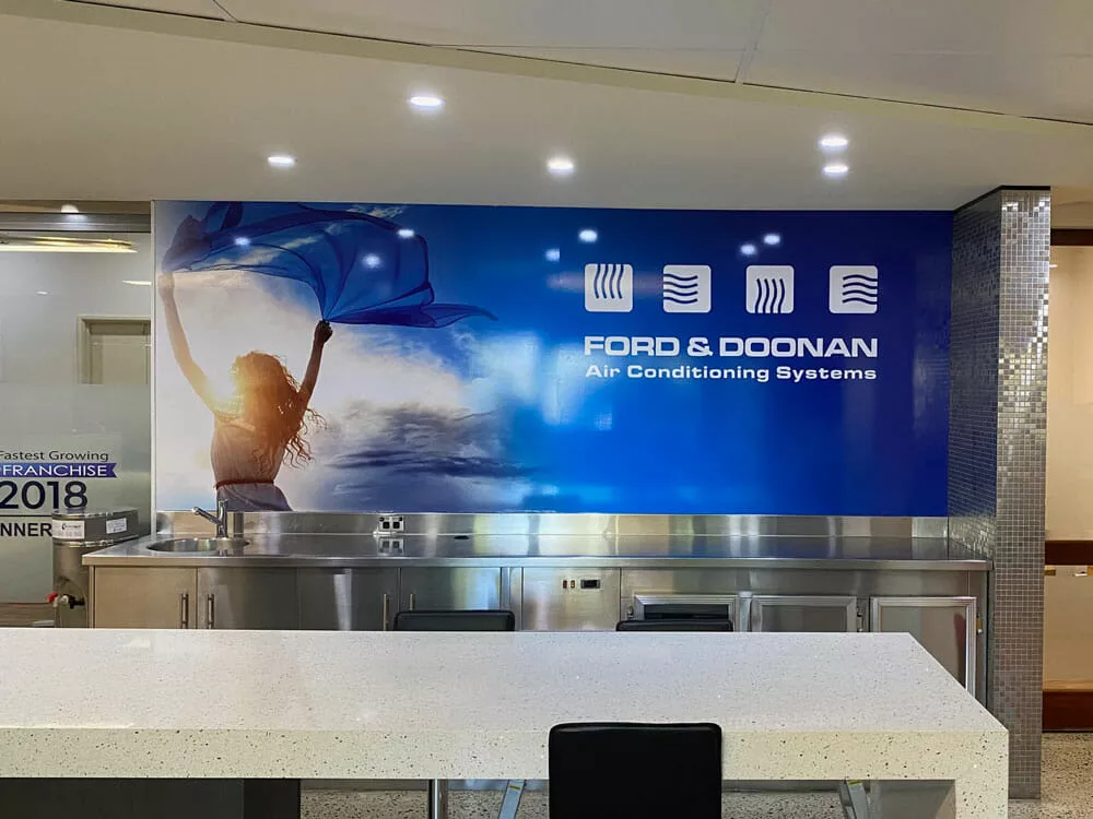 Reception area with a large blue Ford & Doonan Air Conditioning Systems sign. The sign features a silhouette of a woman holding a flowing scarf. Bright and modern atmosphere