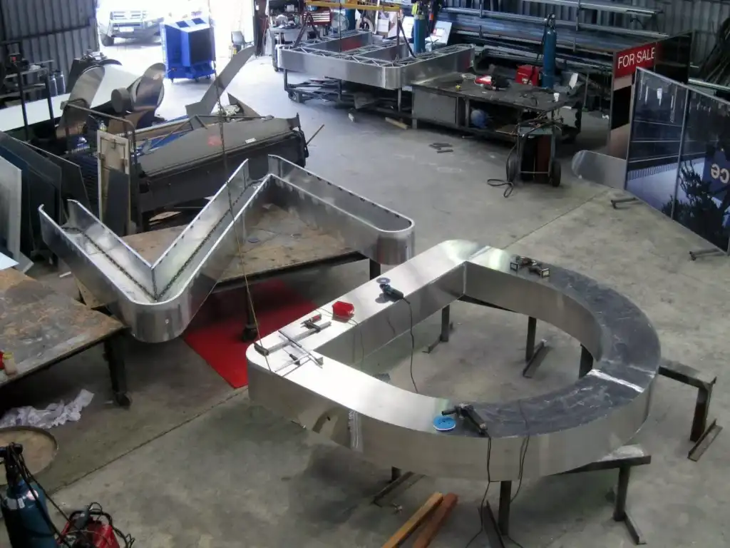 Aerial view of a metal fabrication workshop by Barrett Exhibition Group Perth, showing large shiny metal structures on worktables with tools and equipment around.