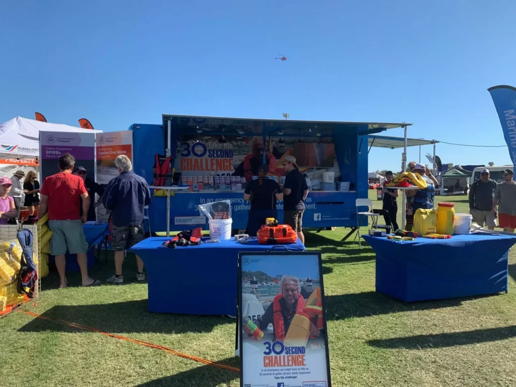 Outdoor safety expo booth featuring "30 Second Challenge" in bold text. Tables display emergency gear; attendees interact under a clear blue sky