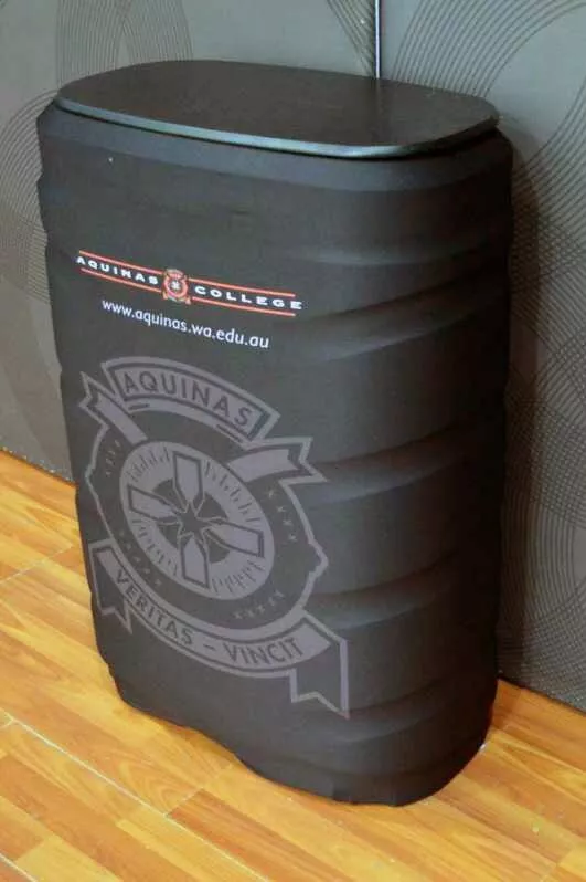 Black cylindricalbin with Aquinas College logo and website, against a patterned wall. Smooth wooden floor