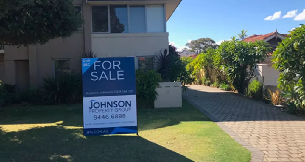 Suburban home with lush greenery, a visible "For Sale" sign by Johnson Property Group at the front. The scene is calm and inviting on a sunny day