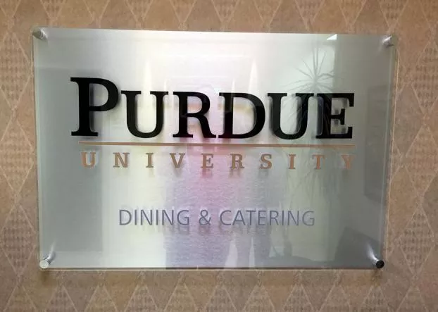 A sign on a textured wall reads "Purdue University Dining & Catering" in bold black letters. It conveys a formal and professional tone