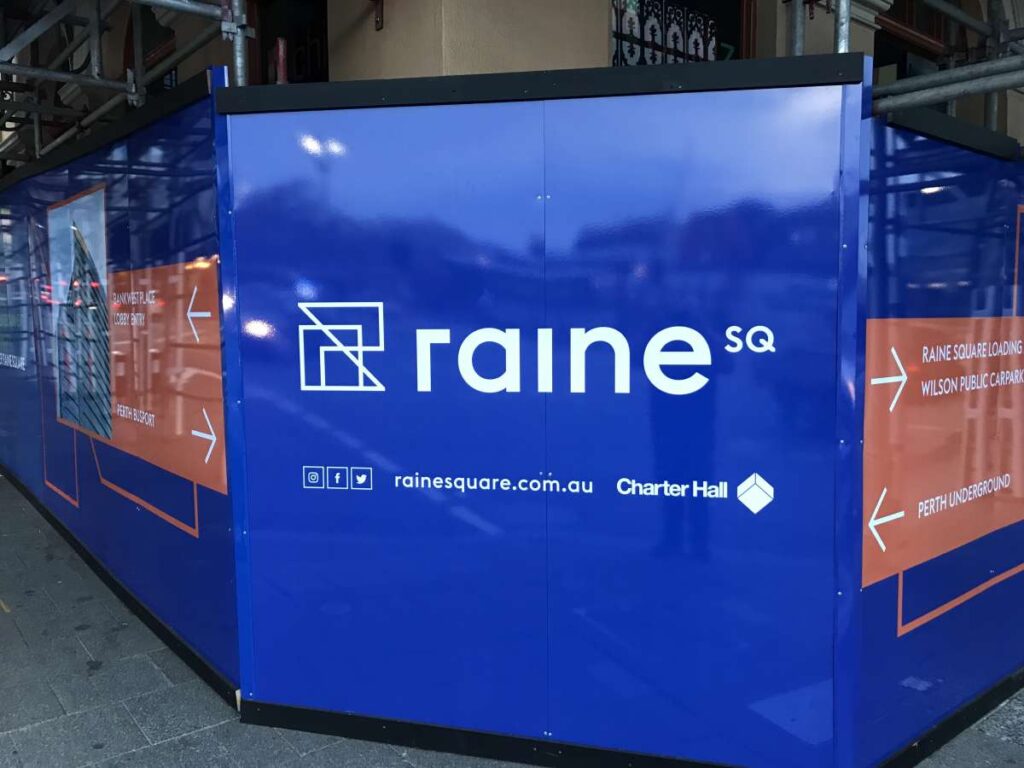 Blue construction hoarding displays the "Raine SQ" logo with arrows indicating directions. Website and social media icons are visible beneath the logo.