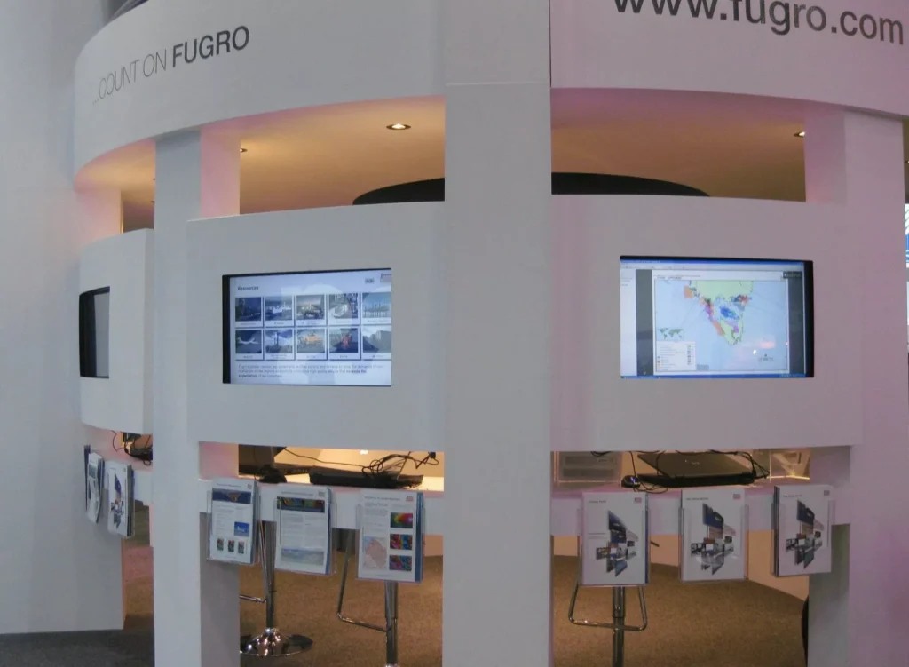 Exhibition booth with dual screens displaying geographical data. Brochures are on racks below