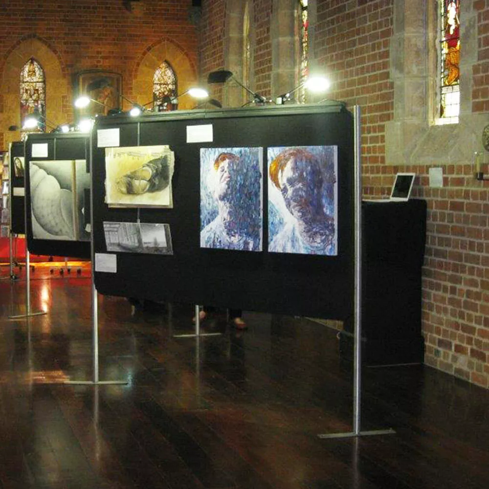 Art exhibition in a brick-walled gallery featuring expressive, textured portraits and abstract pieces. Warm lighting and stained glass windows create a contemplative atmosphere.