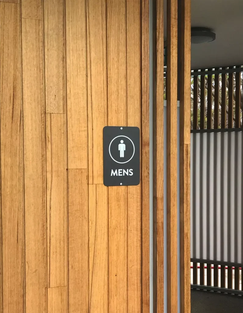 Wooden wall with a "Men's" restroom sign; sign features a male icon. The modern design conveys a clean, welcoming aesthetic