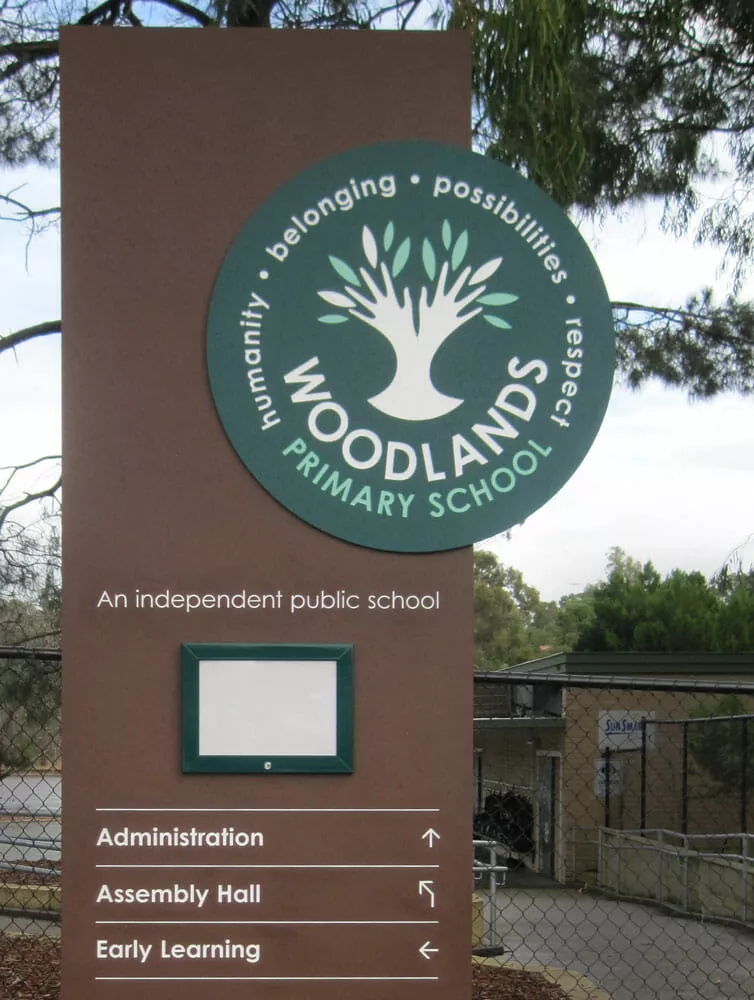 Sign for Woodlands Primary School features a tree logo emphasizing "humanity, belonging, possibilities, respect." Arrows point to Administration, Assembly Hall, and Early Learning