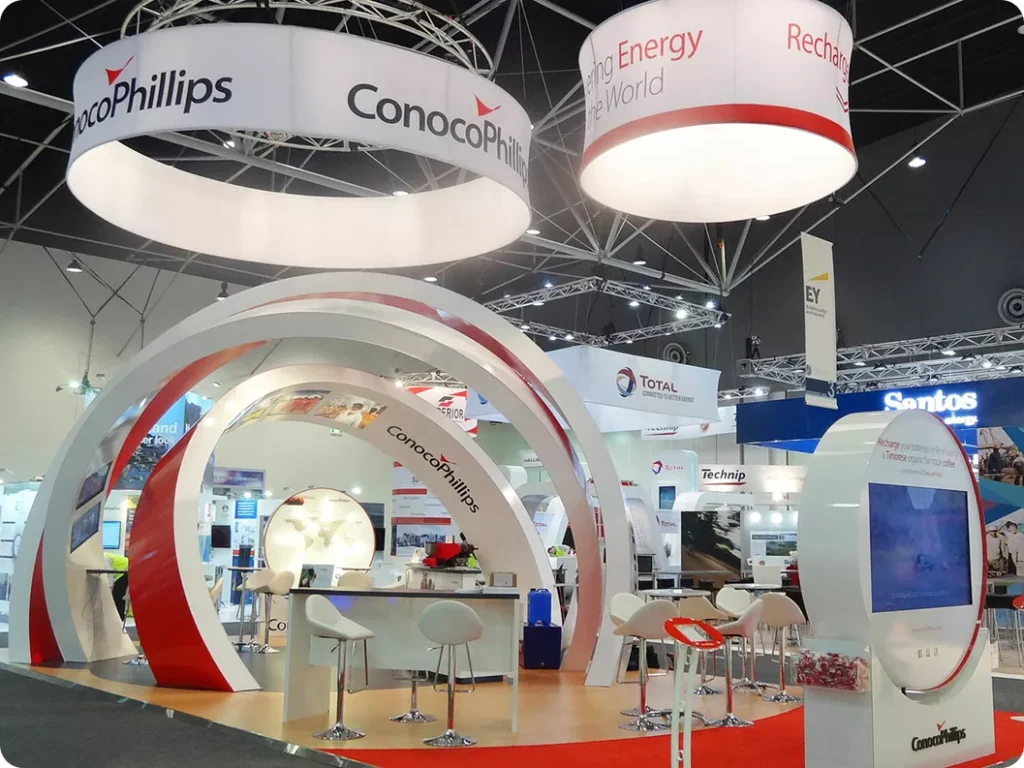 Trade show booth with ConocoPhillips branding. Features white and red arches, modern chairs, and bright lighting, giving a professional, inviting feel.