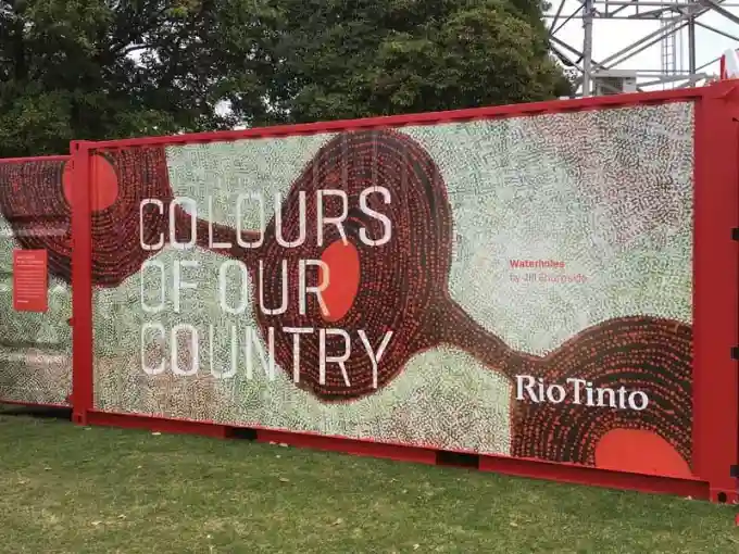A shipping container painted with Aboriginal art features bold earth tones and circular patterns. The text "Colours of Our Country" and "Rio Tinto" is visible.
