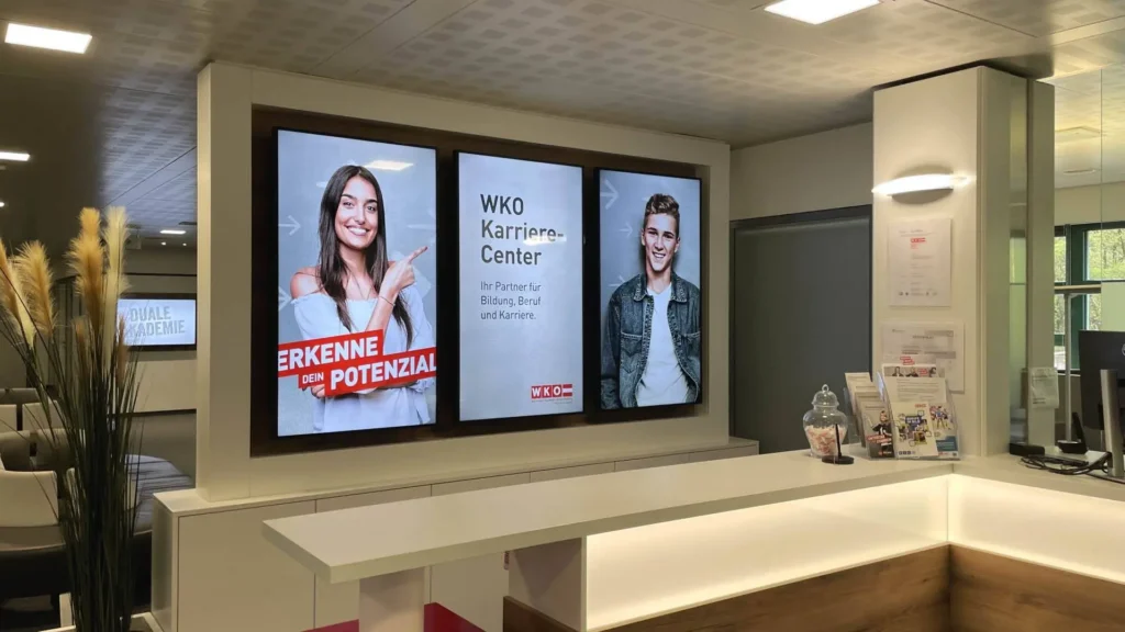 Three vertical digital display screens behind a modern reception desk in a corporate lobby.